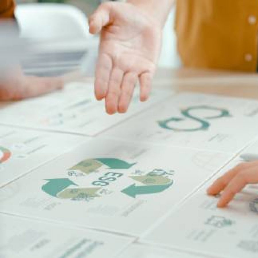 Closeup of team members examine ESG-related documents, pointing and discussing investment strategies for sustainable and renewable energy resources. Eco-Friendly Business Discussing ESG Goals concept.